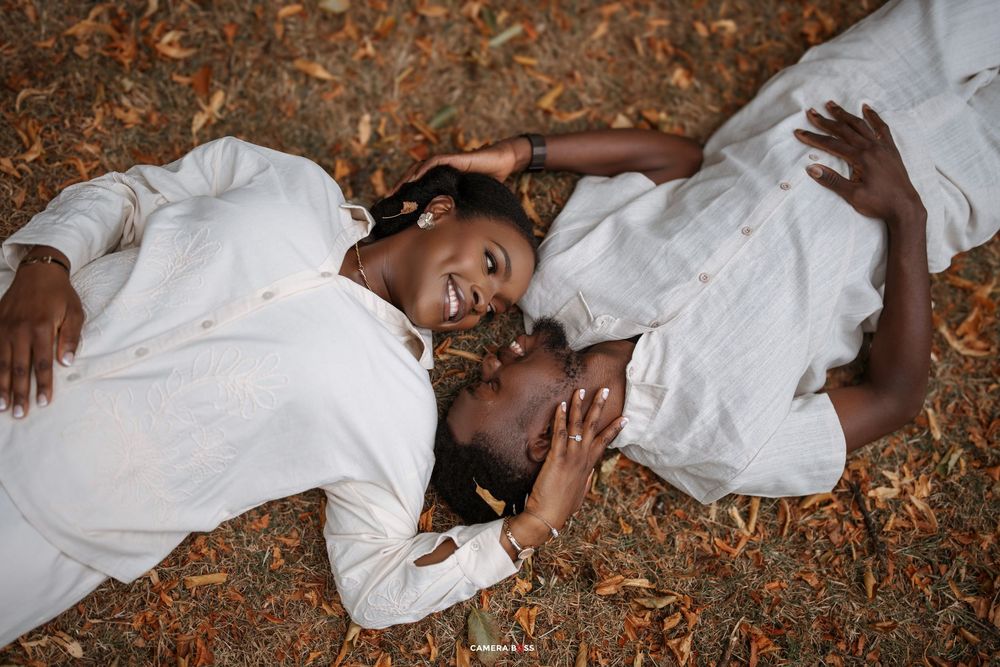 A couple in white clothing lies together on autumn leaves while sharing a tender moment.