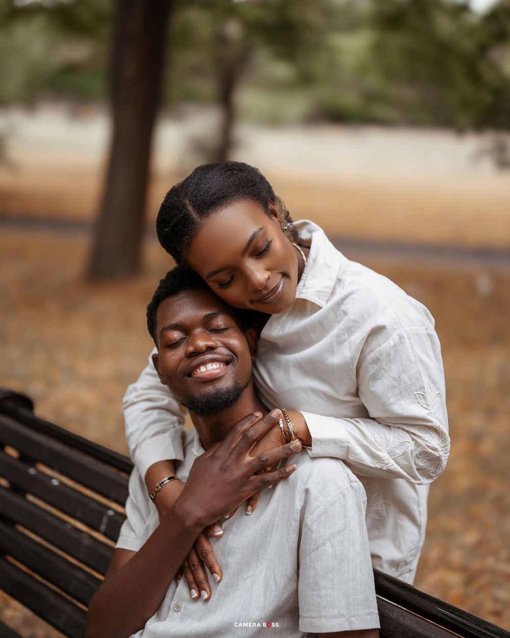 Loving couple in white and grey outfits share tender moments on a park bench surrounded by autumn leaves.