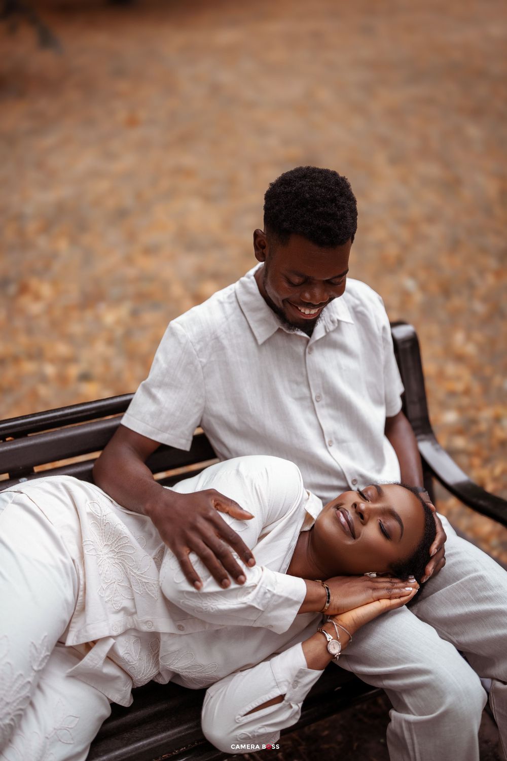 A couple in white outfits share an intimate moment while sitting on a wooden bench outdoors.