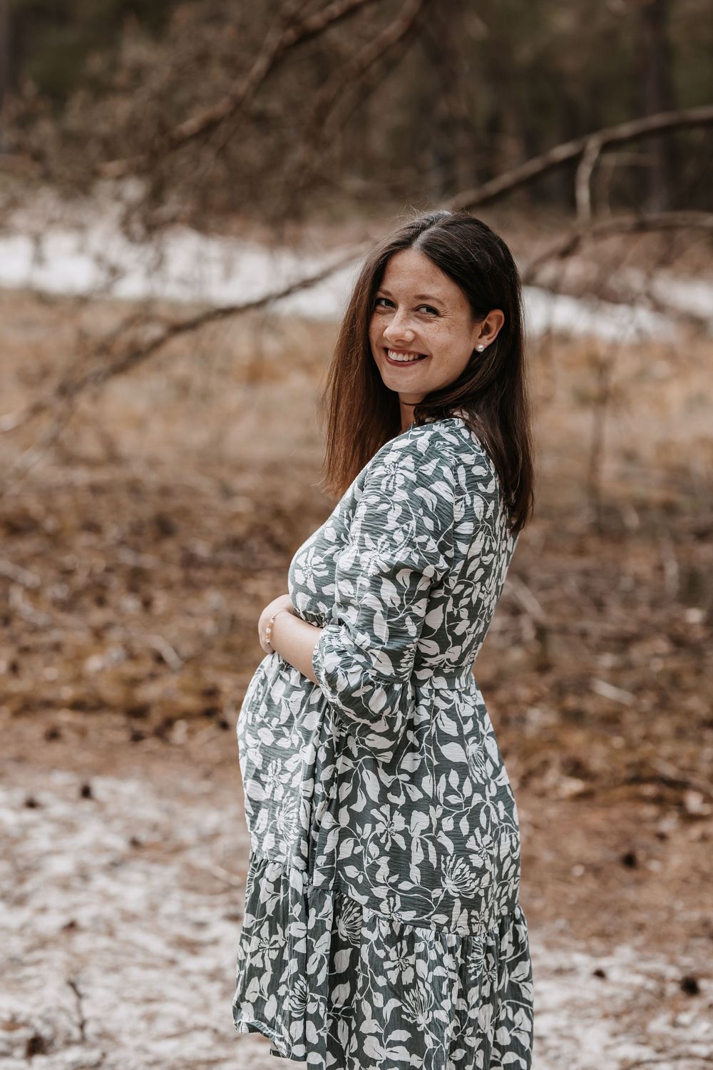 A couple embraces in a forest setting wearing a floral dress and casual attire during an outdoor photoshoot.