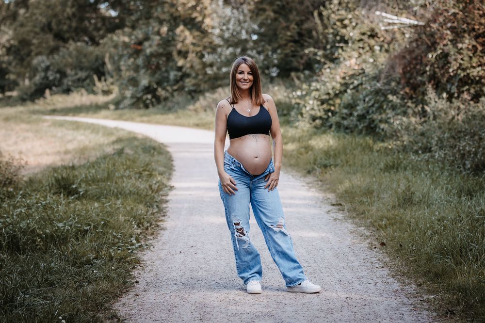 Pregnant woman in casual attire poses confidently on a nature path.