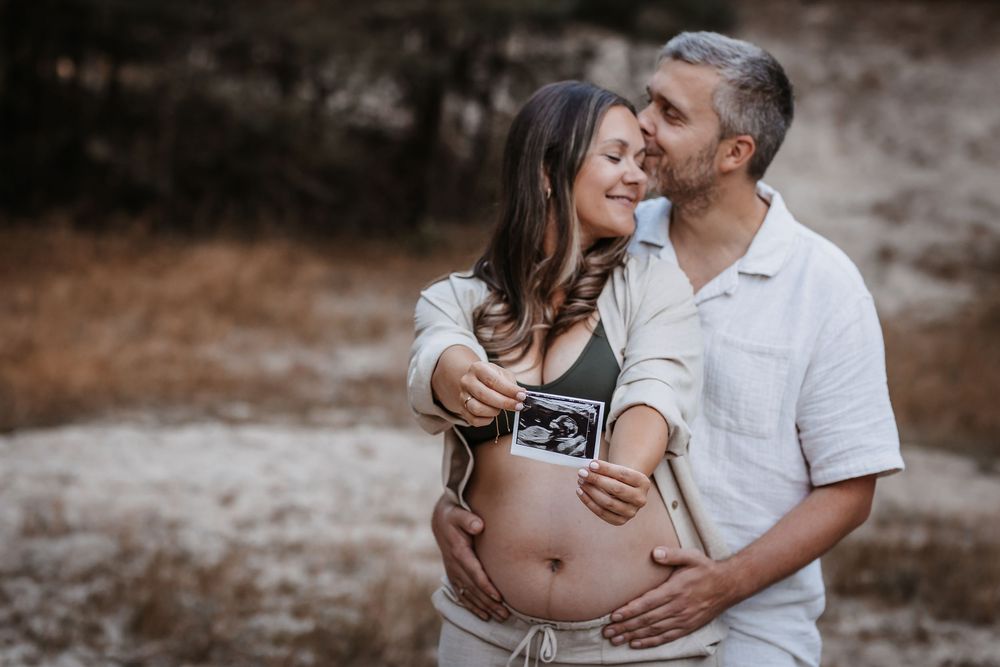 Couple sharing tender moments while holding ultrasound photo outdoors.