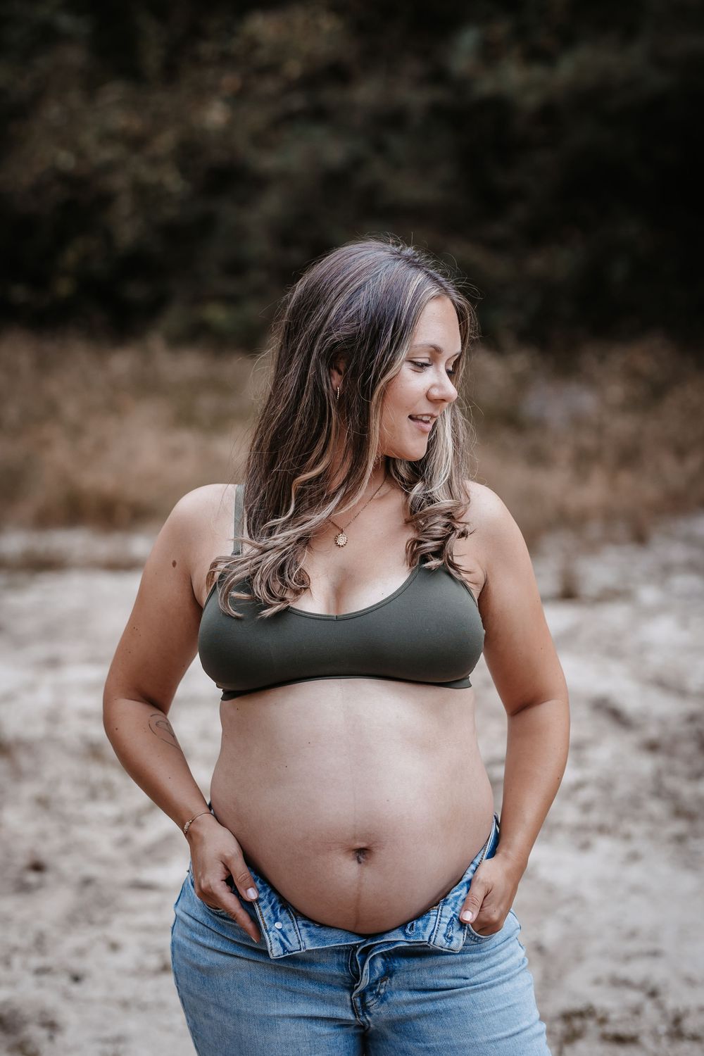 Casual maternity portraits showing pregnant belly against natural backdrop.