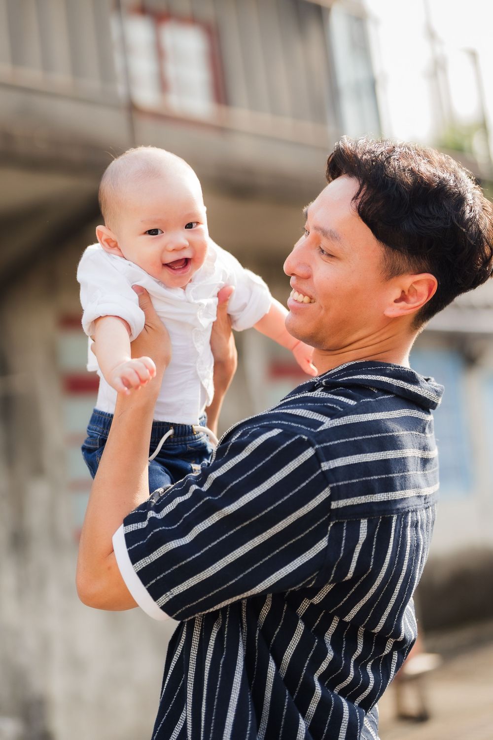 A joyful interaction between a baby in white and an adult in a striped shirt on a sunny day outdoors.