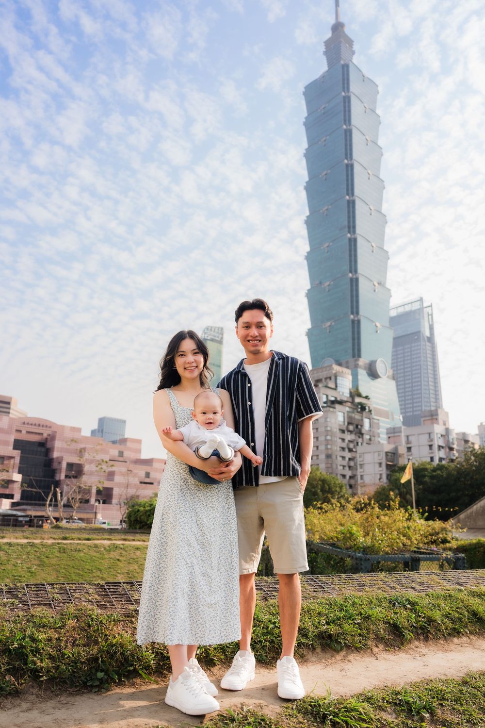 Family portrait series with Taipei 101 skyscraper in background on sunny day with scattered clouds.