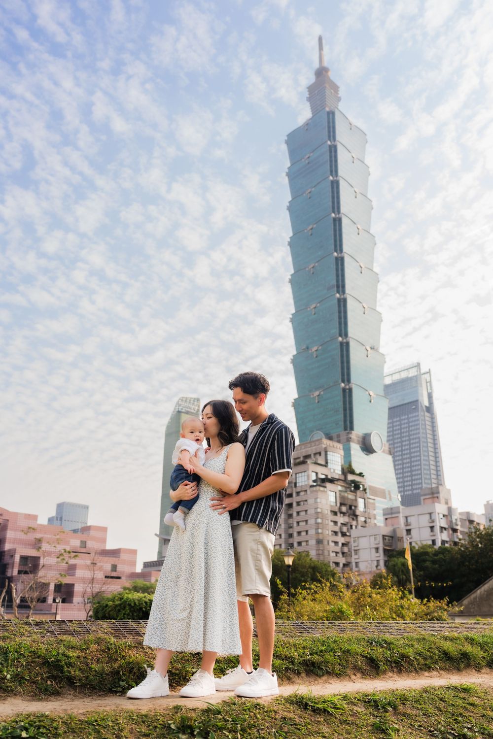 A couple shares a romantic moment with the iconic Taipei 101 skyscraper towering in the background.