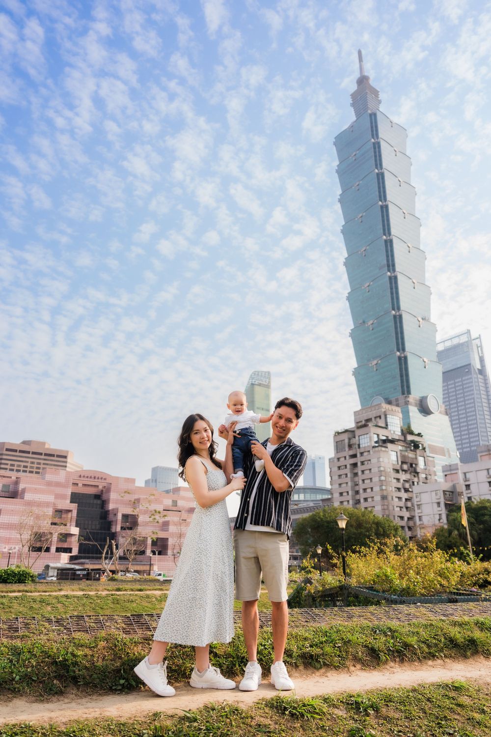 Family photoshoot with Taipei 101 tower in the background under a bright blue sky.