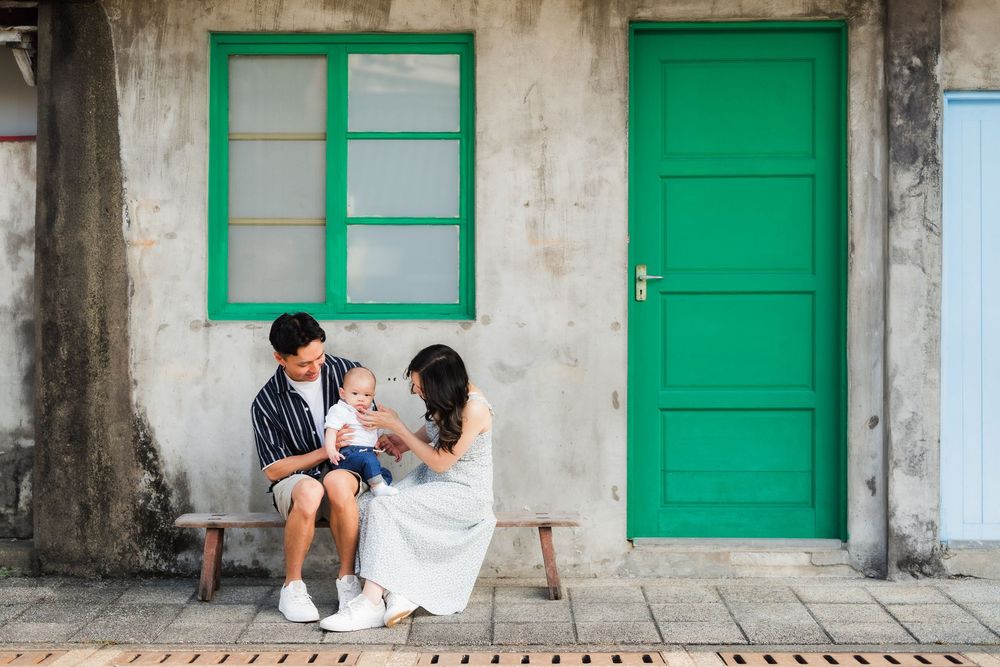 A couple sits together on a bench against a white wall with bright green door and window frames.