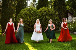 Wedding party in colorful dresses sits casually on grass during outdoor photo session.