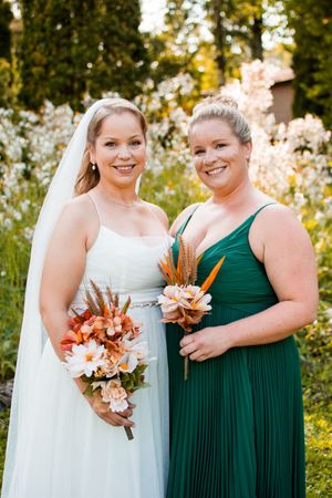 Two people pose with autumn-colored bouquets at an outdoor wedding celebration.