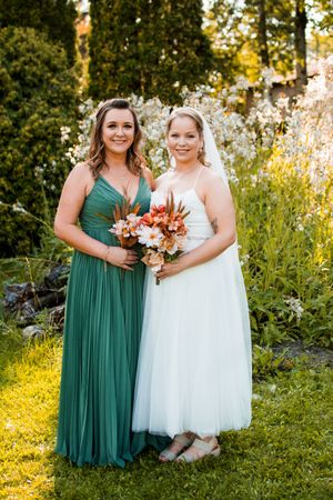 Wedding party members in green and white dresses pose together in a garden setting at sunset.