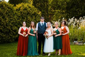 A wedding party poses outdoors wearing alternating red and green formal dresses.