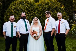 Wedding party poses for formal photos on grass with trees in background.