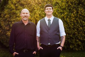 Groomsmen in vests and formal attire standing against lush garden backdrop.