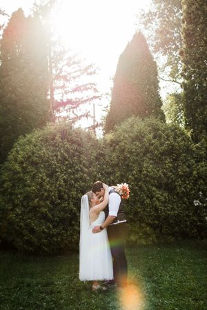 Romantic wedding couple embraces in a sun-drenched garden with lush greenery and beautiful lens flares.