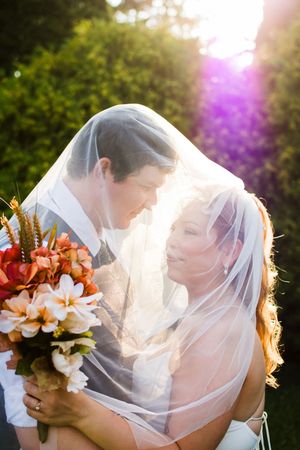 Romantic wedding couple shares intimate moments at sunset with orange lilies in the bridal bouquet.