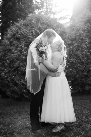 A romantic black and white wedding photo of a couple embracing outdoors with the bride holding a bouquet.