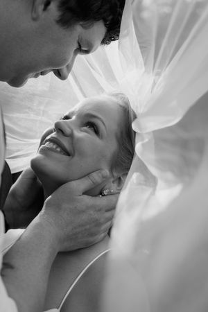 Black and white wedding portraits capture tender moments between newlyweds under a flowing veil.