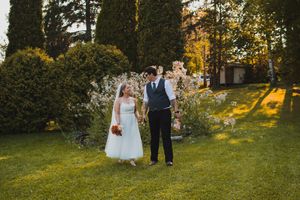 Wedding party poses on lush green lawn during golden hour with trees in background.