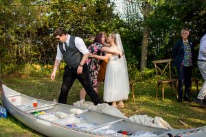 Newlyweds carefully step into a canoe filled with decorations during their outdoor wedding celebration.