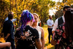 Wedding celebration during golden hour with guests mingling under autumn trees.