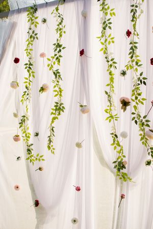 White fabric backdrop decorated with hanging greenery and roses creates an elegant wedding ceremony setting.