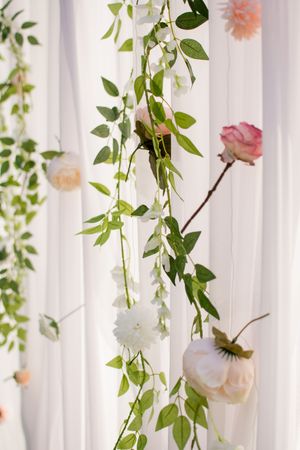 Elegant white curtain backdrop decorated with hanging floral arrangements and greenery for a wedding ceremony.