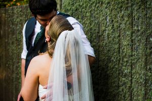 A wedding couple poses against a rustic wooden wall in natural lighting.
