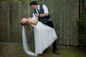 A romantic wedding dip pose against a wooden fence backdrop in a garden setting.
