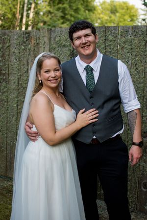 A wedding couple poses together in front of a wooden fence during an outdoor photo session.