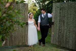 Wedding couple walking through rustic wooden fence pathway in garden setting.