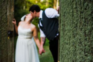 Wedding party gathered in front of lush green hedge during outdoor celebration.