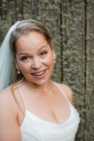A joyful bride wearing a white wedding dress and veil poses against a floral backdrop.