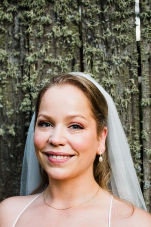 A bride in a white dress and veil smiles radiantly in an outdoor portrait session.