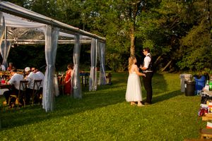 Outdoor wedding venue with white tent and guests on grassy hillside.