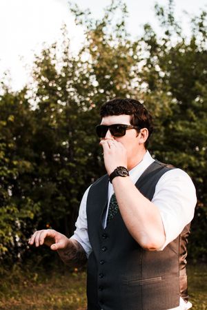 Wedding guest in formal attire gestures emotionally during outdoor reception.
