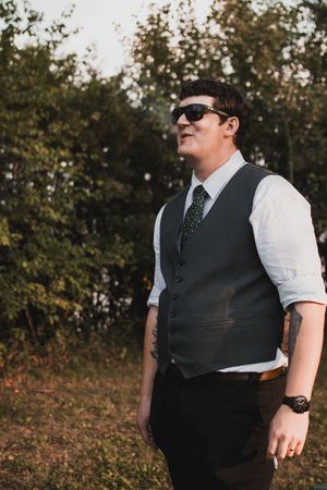 Groomsmen in dark vests and sunglasses pose casually during outdoor wedding.