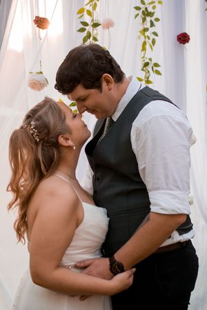 Intimate wedding couple shares romantic kisses against a white curtain backdrop with hanging flowers.