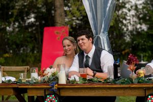 Wedding reception dinner setup with long tables under clear tent canopy and floral centerpieces.