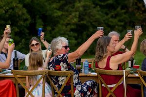 Wedding guests toast and celebrate at outdoor reception with wooden benches.