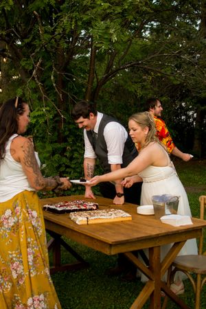 Wedding guests enjoy pizza served on rustic wooden tables at an outdoor reception.