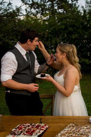 A couple shares cake at their wedding reception outdoors.