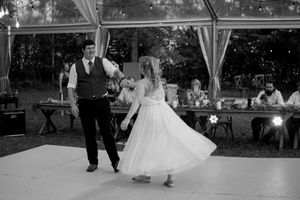 Wedding reception dance floor with guests dancing under white tent and string lights.