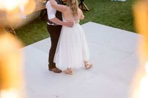 Couple dances on white dance floor during outdoor wedding reception at sunset.