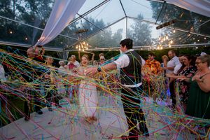 Wedding celebration under clear tent with colorful streamers flying through the air as couple dances on illuminated dance floor.
