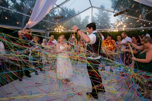 Colorful streamers fill the air as wedding guests celebrate under tent during reception.