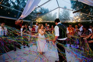 Colorful streamers fill the air as a couple dances under a clear tent at their wedding reception.