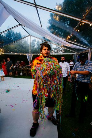 Wedding reception celebration with colorful streamers and dancing under a clear tent at dusk.