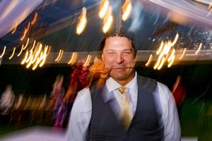 Wedding reception tent glows with warm lighting as guests dance and celebrate.