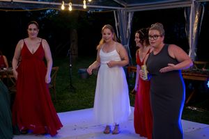 Wedding reception guests dance and celebrate under string lights and white tent covering.